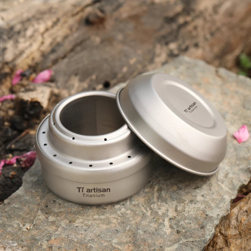 Titanium container with lid on a rocky surface, featuring 'Ti artisan' branding.