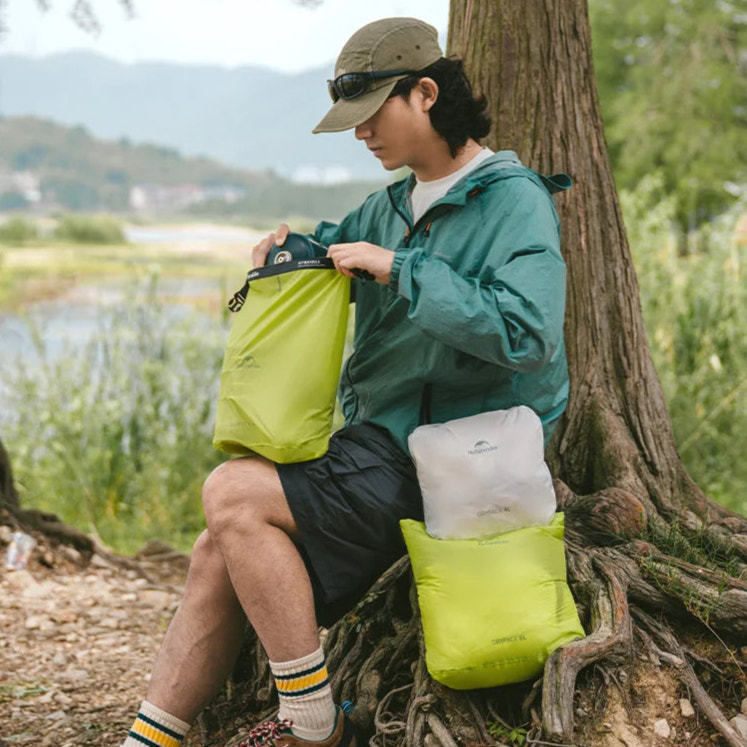 Person sitting by a tree with camping gear in a natural setting