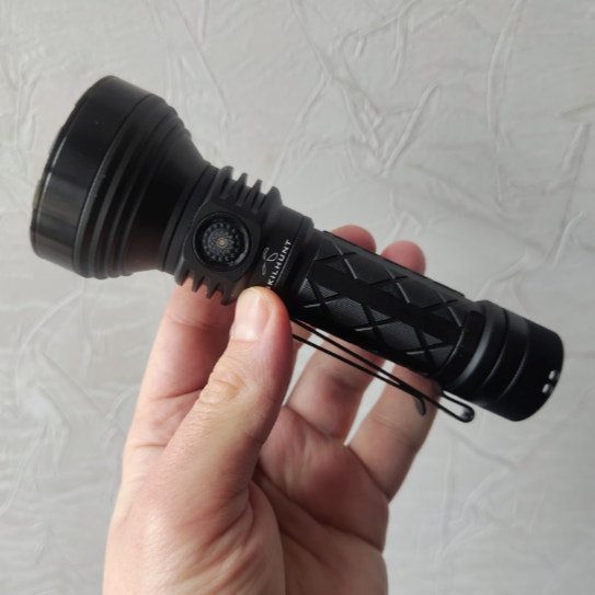 Black flashlight held in a hand against a light gray background