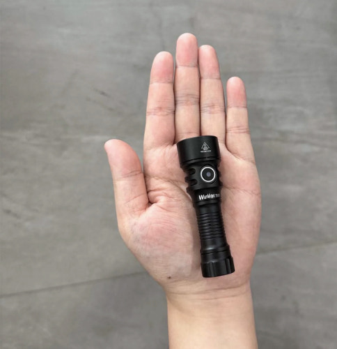 Black flashlight held in a hand against a gray background