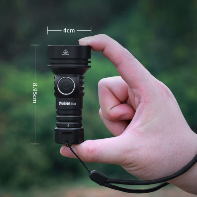 Hand holding a black flashlight with measurements indicated, against a blurred green background