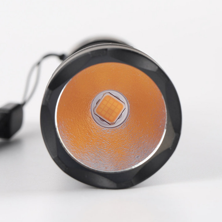 Close-up of a round flashlight with orange lens and black casing on a white background