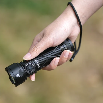 Hand holding a black flashlight with a blurred natural background