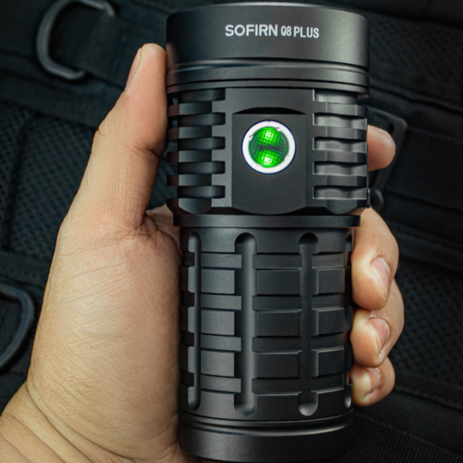Black SOFIRN Q8 PLUS flashlight held in a hand against a dark background
