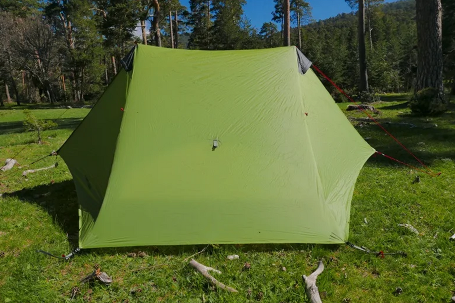 Green camping tent set up in a forest with trees and grass in the background