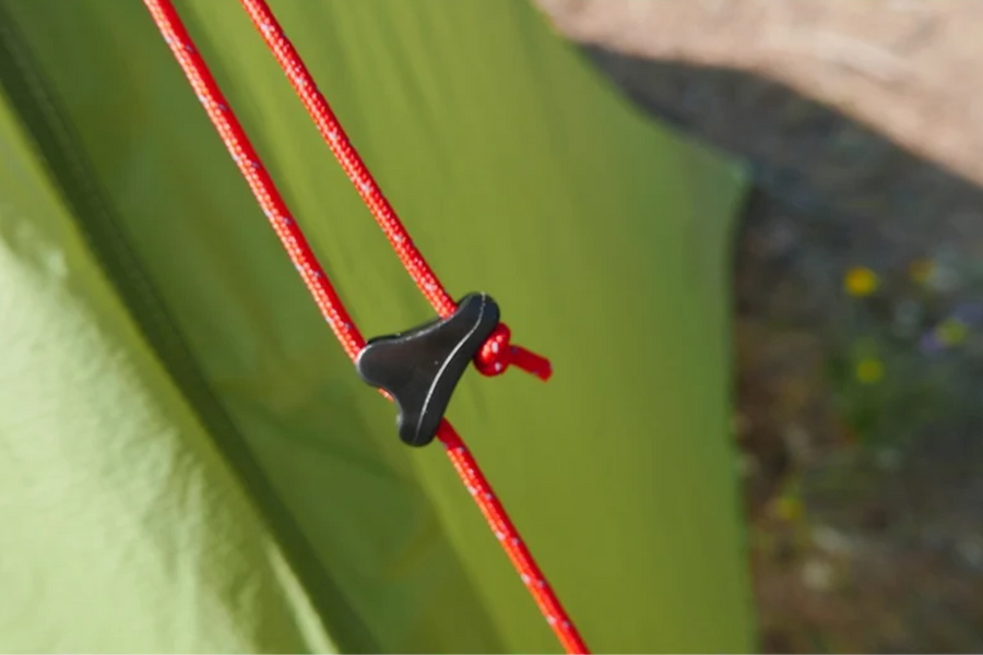 Close-up of a green tent with red ropes and black plastic knotter.