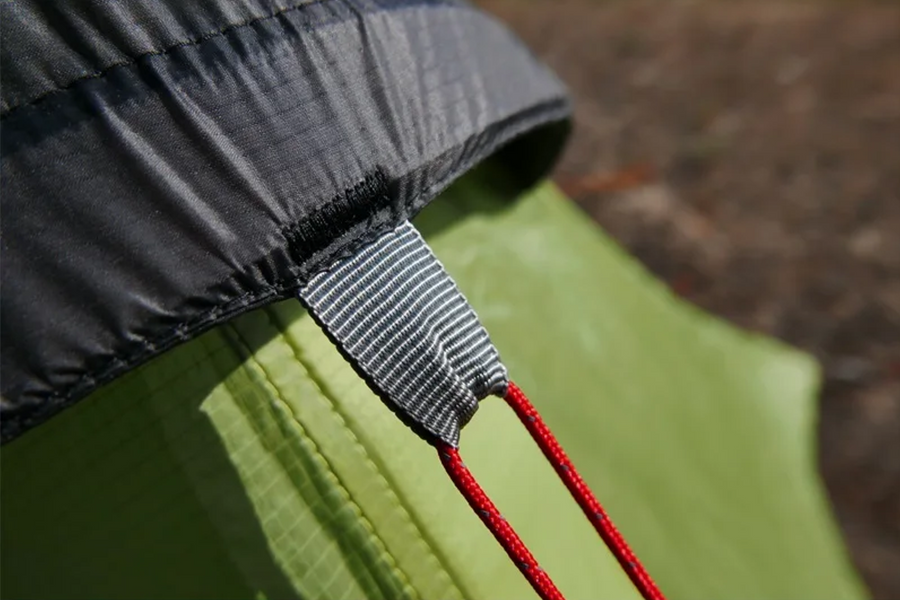 Close-up of a tent zipper with red pull tab on a green and black tent fabric.