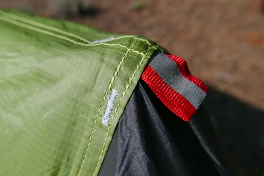 Close-up of a green fabric with a red and gray strap, possibly from a tent or outdoor equipment.