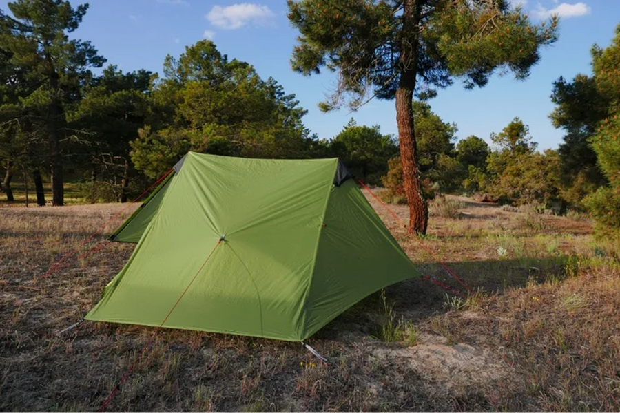 Green tent set up in a forest clearing with trees and blue sky.