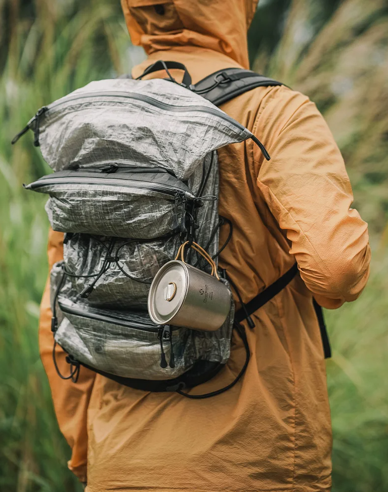 Person wearing a backpack with a can attached, standing in a natural setting.