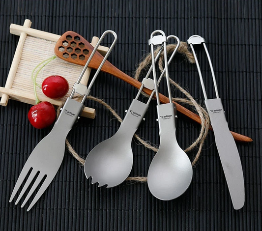Set of titanium cutlery including fork, spoon, and knife on a dark surface with wooden utensils and cherries.