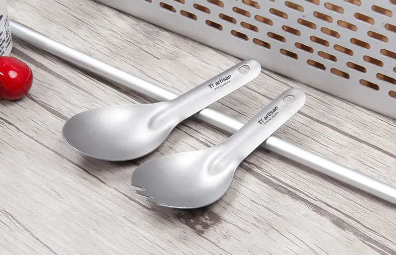 Two titanium spoons on a wooden surface with a white basket in the background.