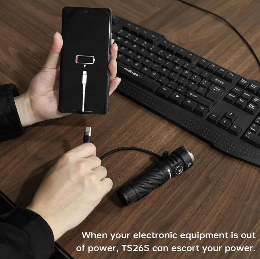 Person plugging a phone into a flashlight with a keyboard in the background on a wooden desk.