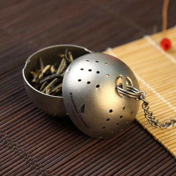 Tea ball infuser with tea leaves on a wooden surface