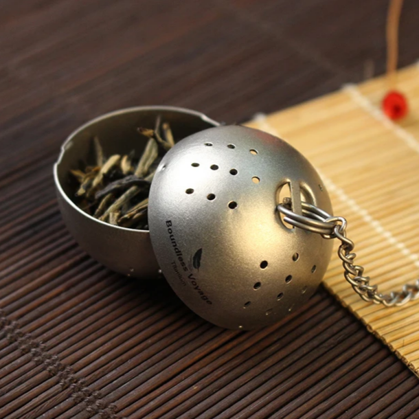 Tea ball infuser with tea leaves on a wooden surface