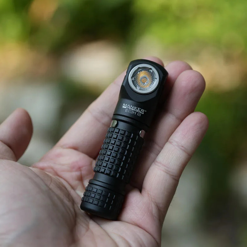 Hand holding a black flashlight with a blurred natural background