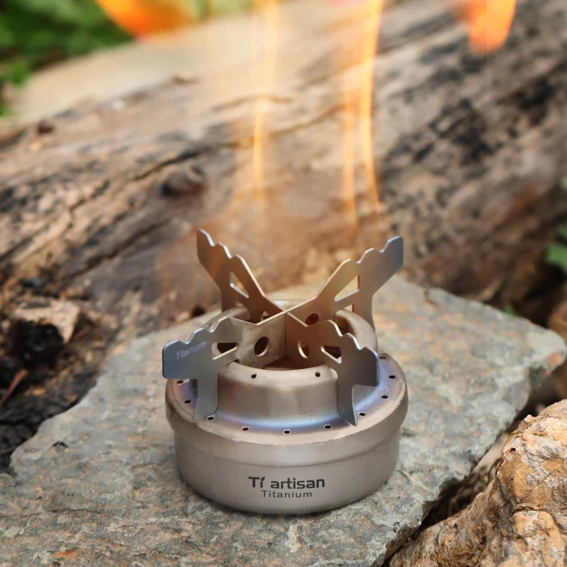 Titanium camping stove on a rock with flames in the background