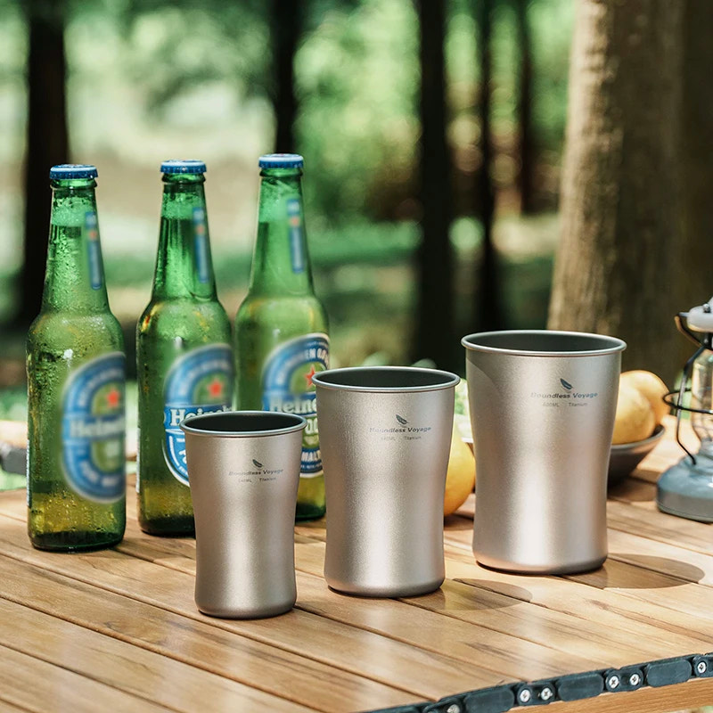 Metal cups and beer bottles on a wooden table with a forest background