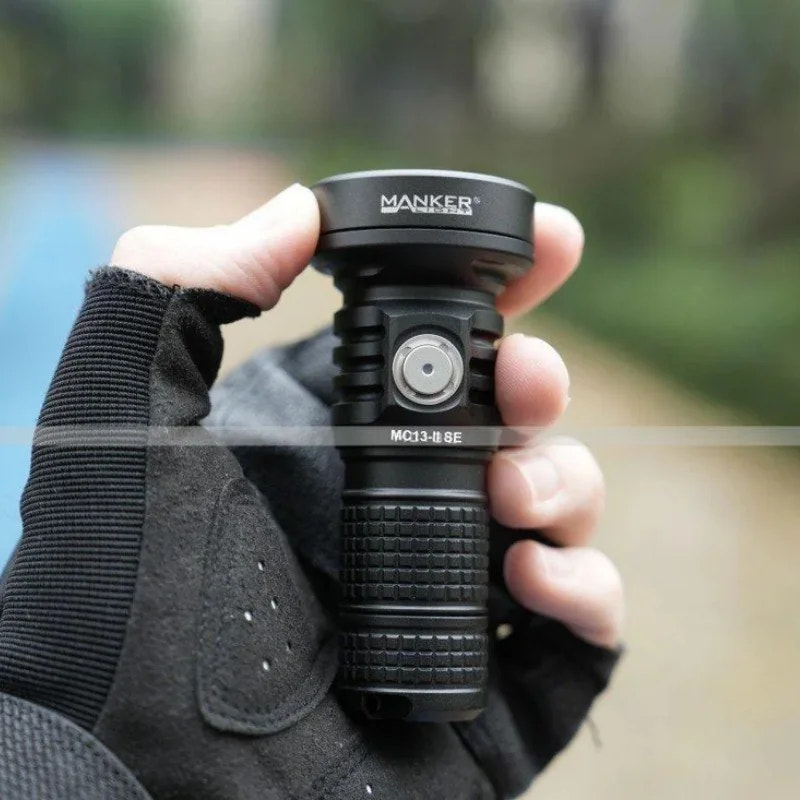 Hand holding a MANKER flashlight with a blurred background