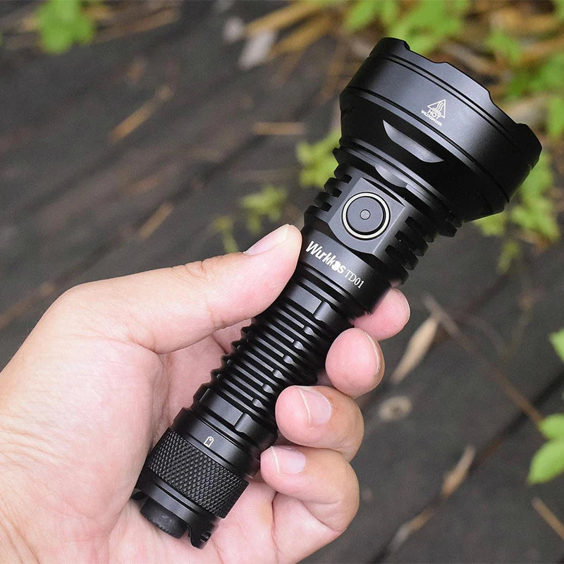 Hand holding a black flashlight with a blurred natural background