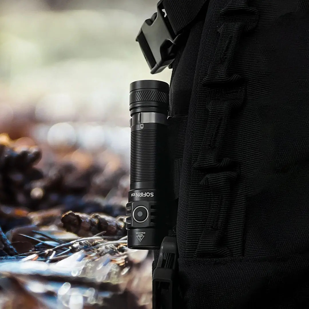 Black flashlight attached to a person's gear with a natural background
