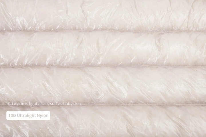 Close-up of a white quilt with text indicating '100 Ultralight Nylon' and 'Light as Air, Soft as Baby Skin'.
