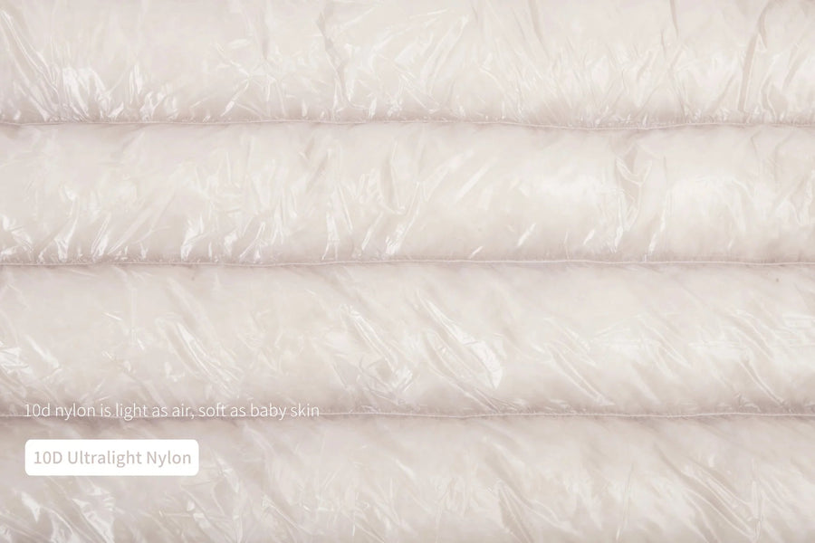 Close-up of a white quilt with text indicating '100 Ultralight Nylon' and 'Light as Air, Soft as Baby Skin'.