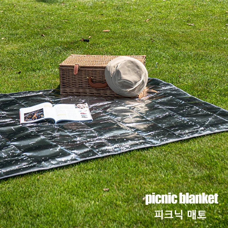 Picnic blanket with a picnic basket, hat, and open book on grass