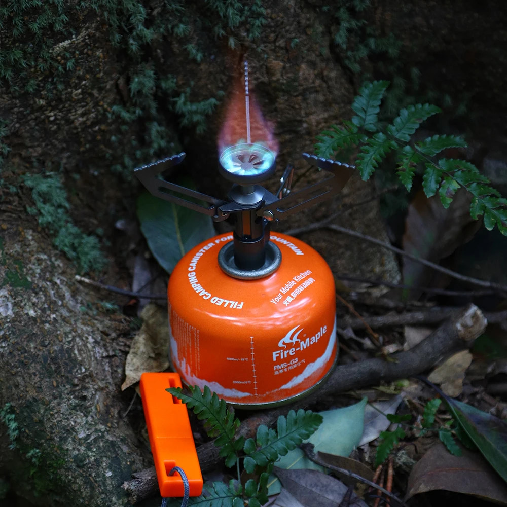 camping stove with visible flame surrounded by green foliage