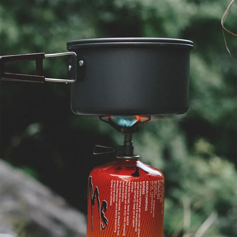 Black camping pot on a red gas canister with a blurred green background